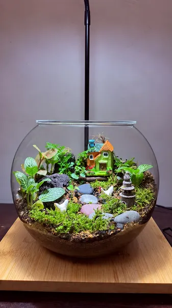 Fishbowl terrarium with a tiny cottage, hens, river stones, a lantern and fittonia